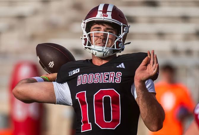 Josh Hoover winds up to throw in a black Indiana Hoosiers jersey, number 10, during pregame warmups.